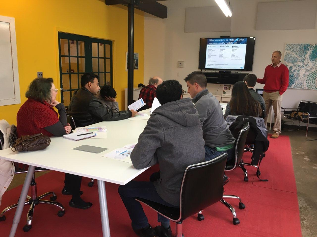 A facilitator guiding a seated group through a slide on sensations and responses during a HEAL training session