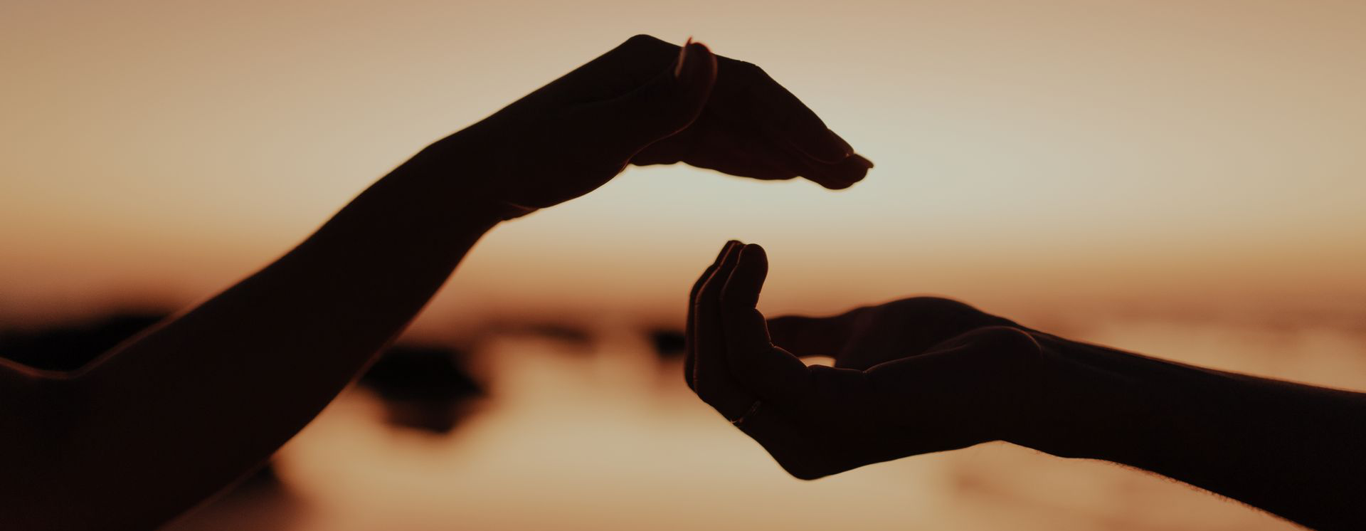 Two hands reaching toward each other in front of a warm sunset — photograph by Jonathan Borba